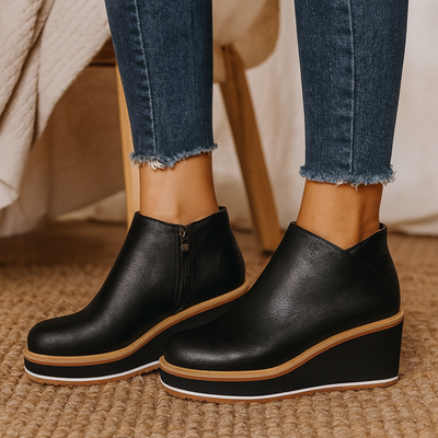 Black wedge ankle boots worn with blue jeans on a textured surface.