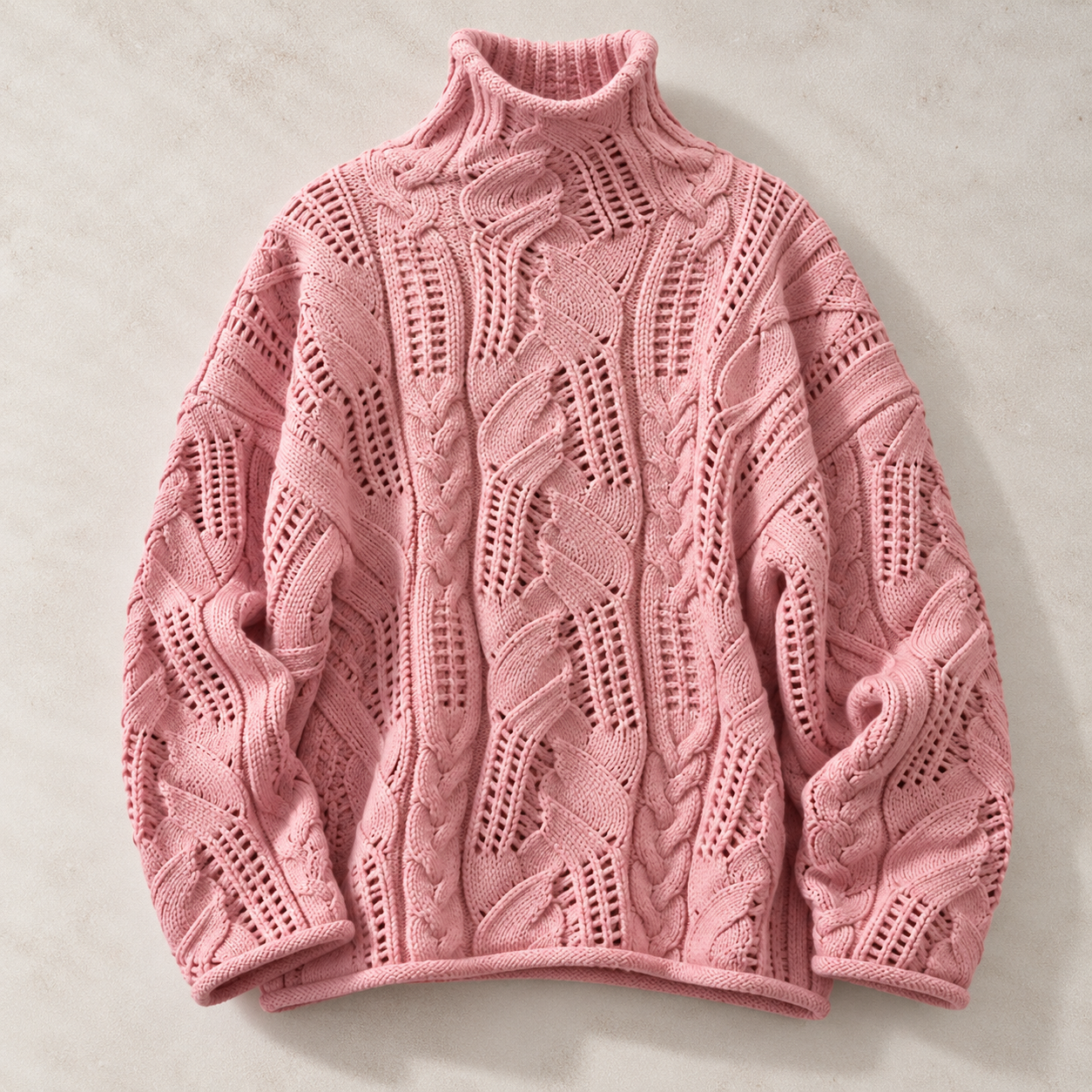 A pink cable-knit turtleneck sweater with a textured, openwork pattern, laid flat on a light beige background.