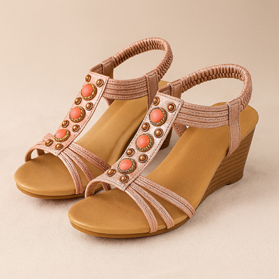 Pair of tan wedge sandals with pink straps and decorative elements on a beige background