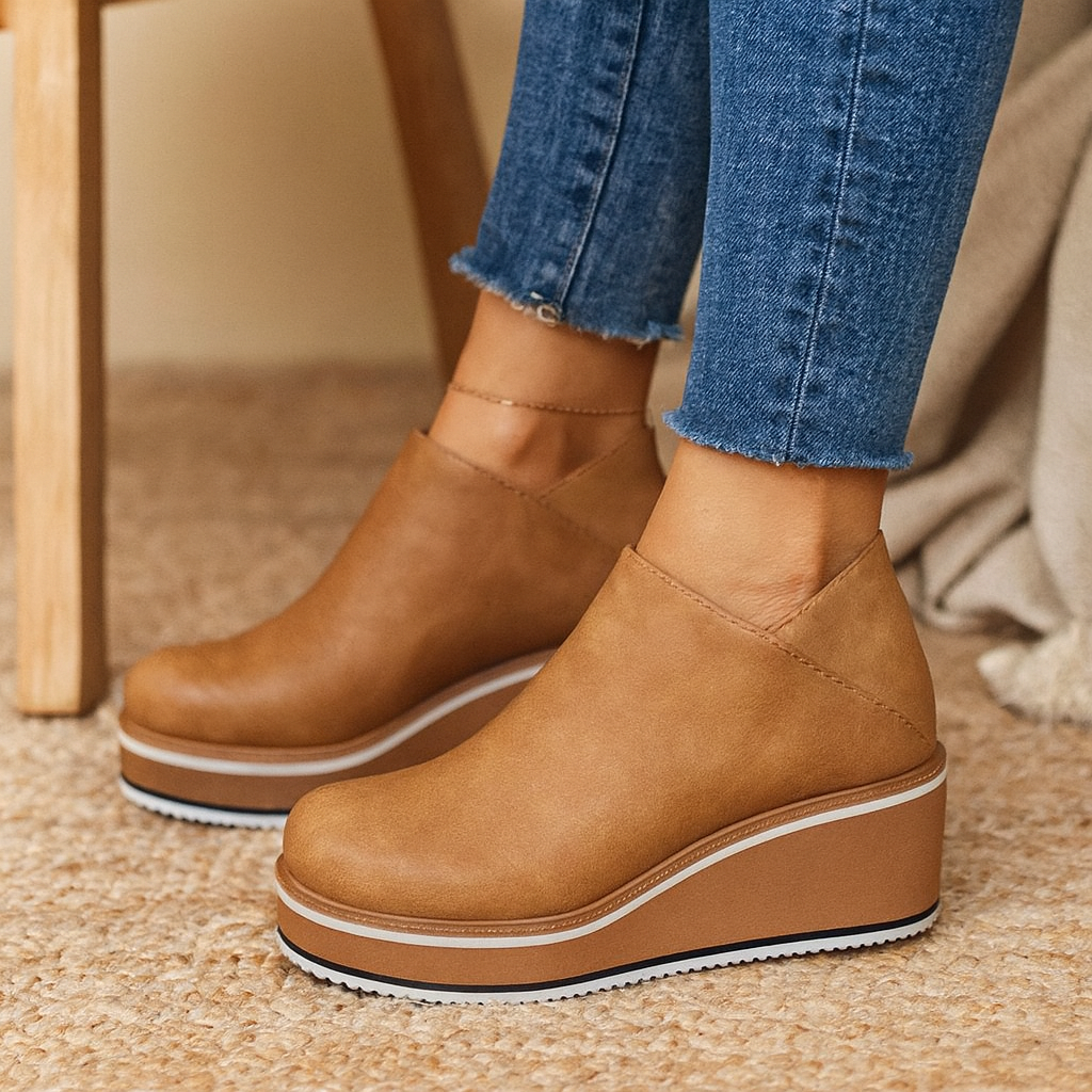 Brown wedge shoes worn with blue jeans on a carpeted floor.