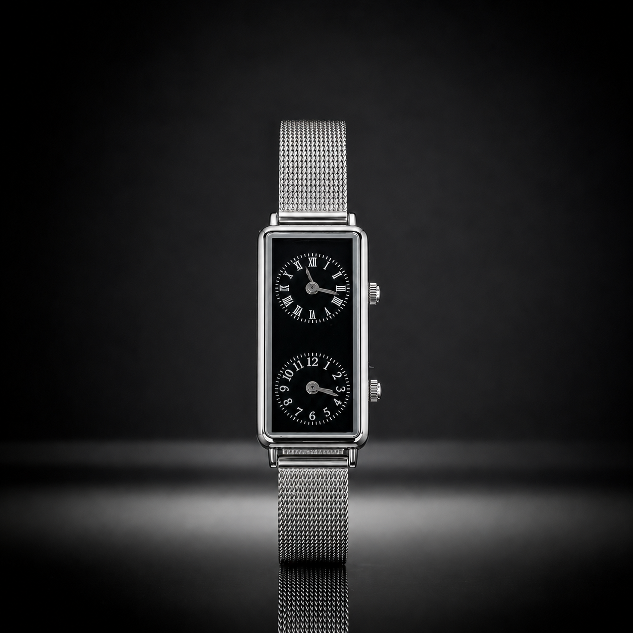 A rectangular silver-tone watch with a black dial and two nested sub-dials, mounted on a silver mesh strap, set against a dark gradient background.