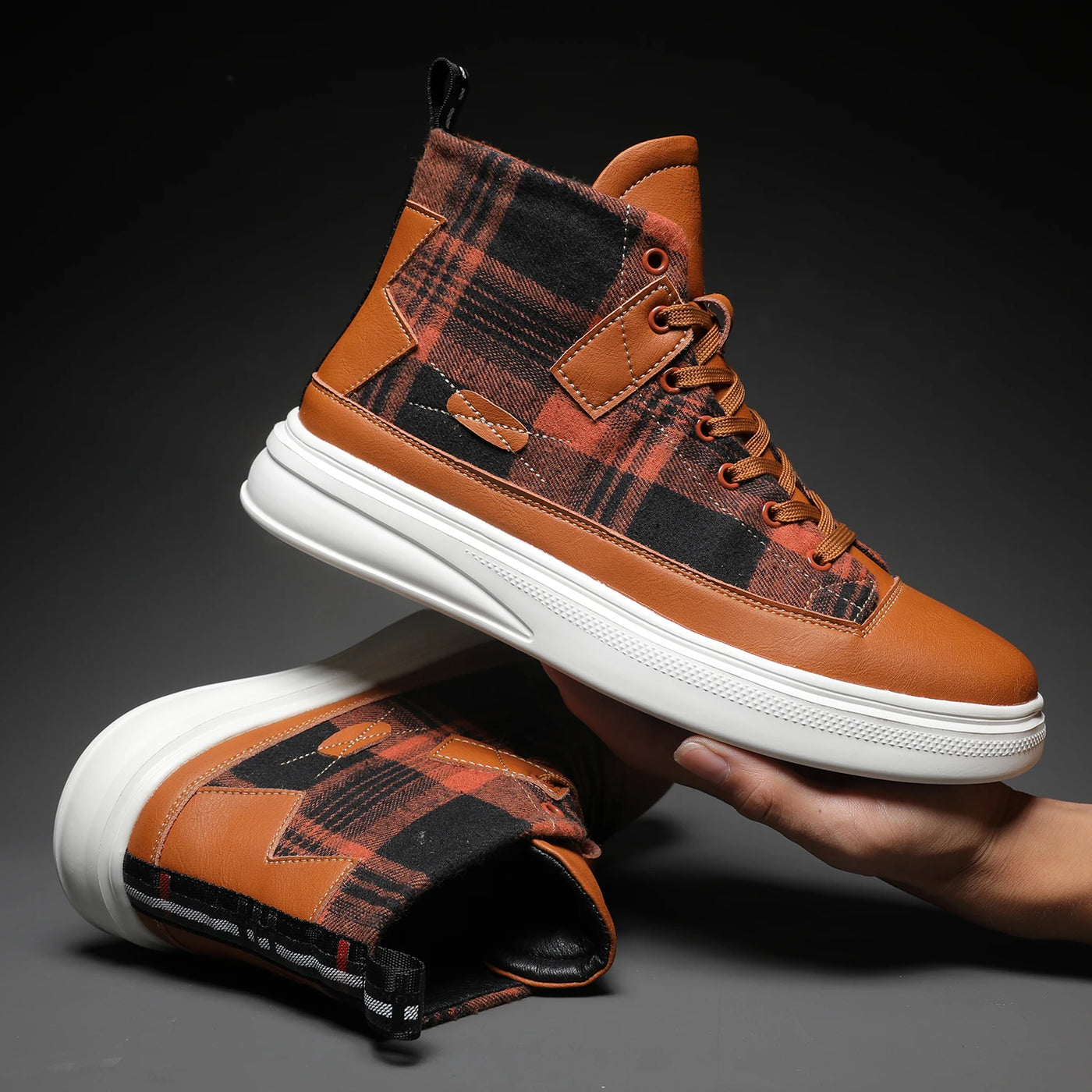 Brown and black plaid high-top sneakers with white soles held by a hand on a dark background