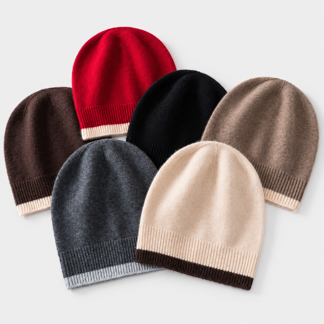 Six knit beanie hats in different colors, arranged in a fan-like layout on a light gray background. The hats are red, brown, black, taupe, charcoal, and cream, each featuring a contrasting ribbed band at the bottom.