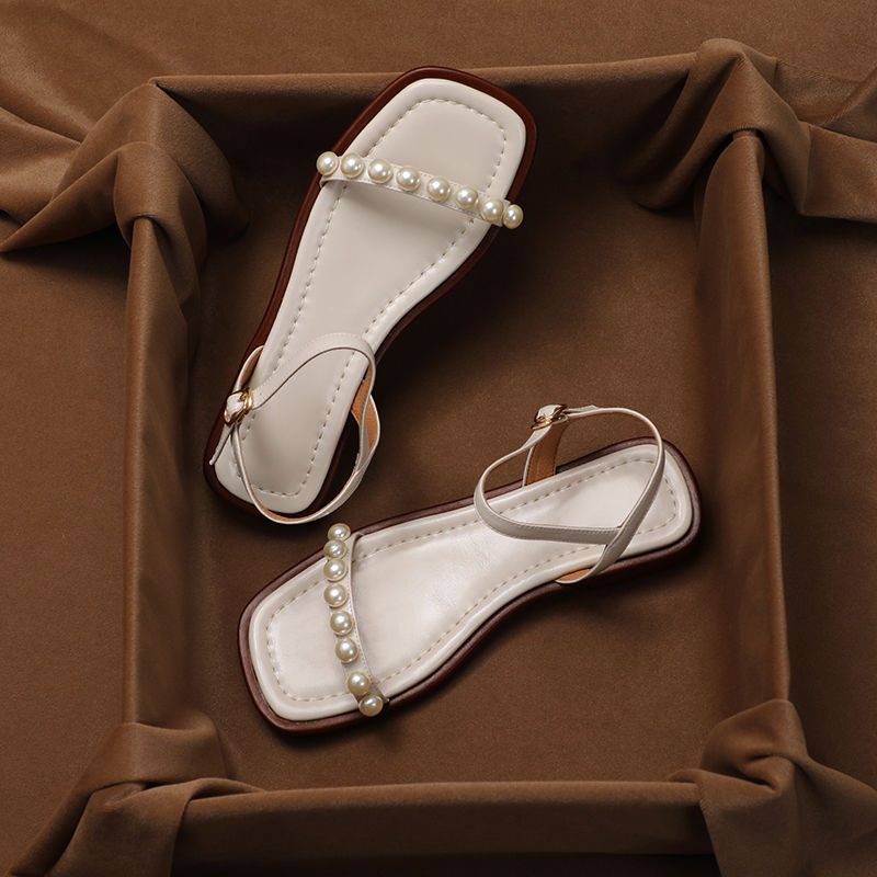Pair of white sandals with pearl embellishments on a brown fabric background