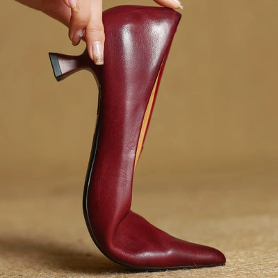Maroon high-heeled shoe held by a hand against a beige background
