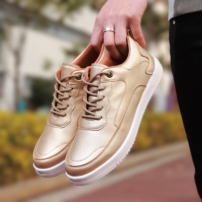 Gold sneakers with white soles held by a hand against a blurred outdoor background