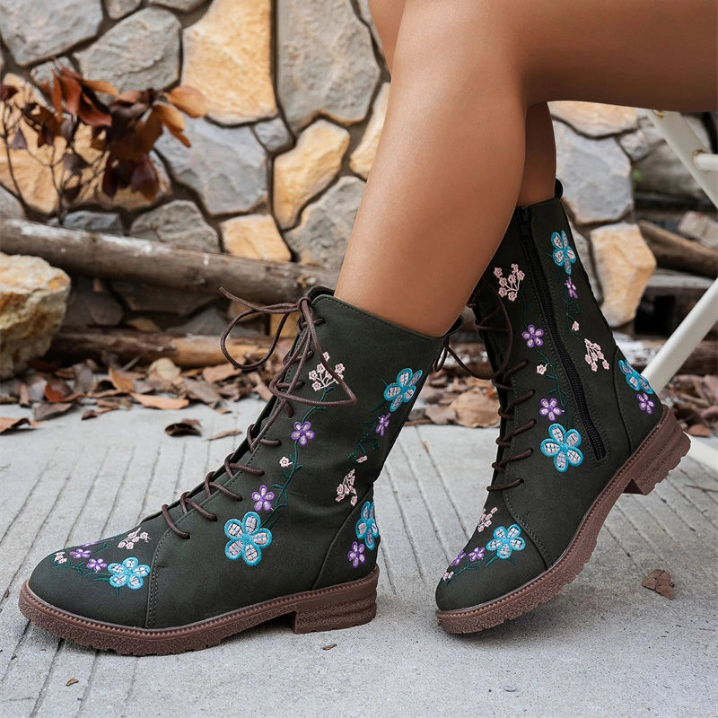 Black lace-up boots with floral embroidery on a stone and concrete background