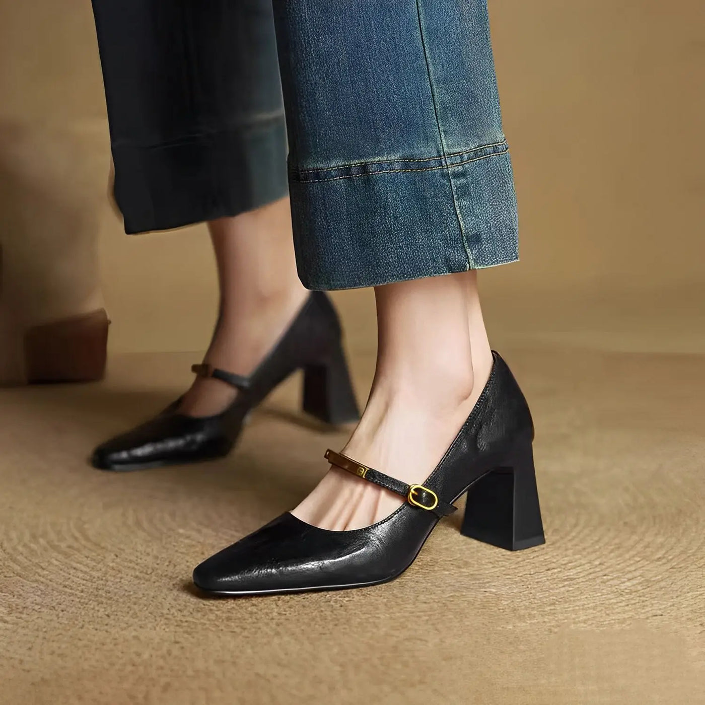 Black high-heeled shoes with a strap worn by a person on a beige background