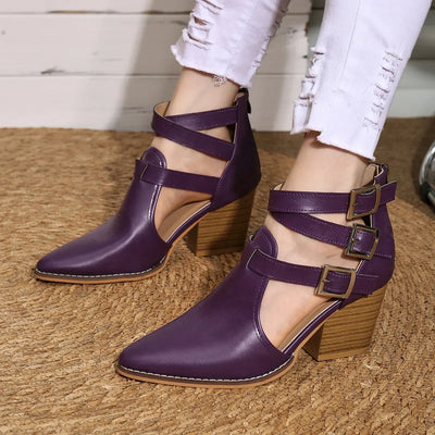 Purple high-heeled shoes with cut-out design worn by a person on a textured surface.