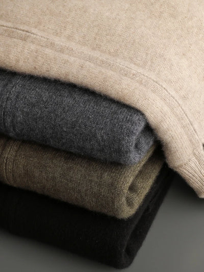 Stack of folded cashmere sweaters in beige, gray, brown, and black on a neutral background