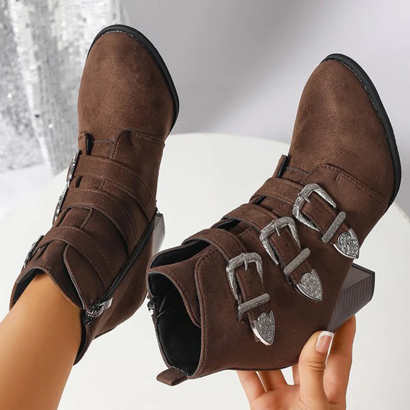 Brown suede boots with silver buckles held against a white background
