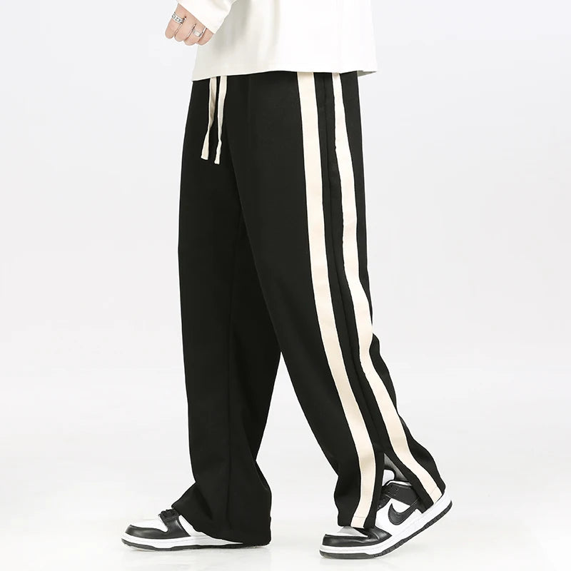 Black track pants with white stripes worn by a person on a white background