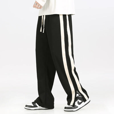 Black track pants with white stripes worn by a person on a white background