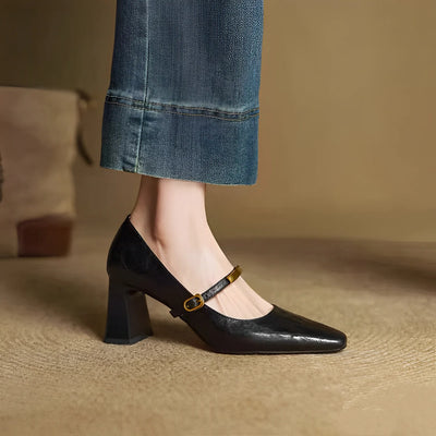 Black shoe with a gold strap worn with blue jeans on a beige background