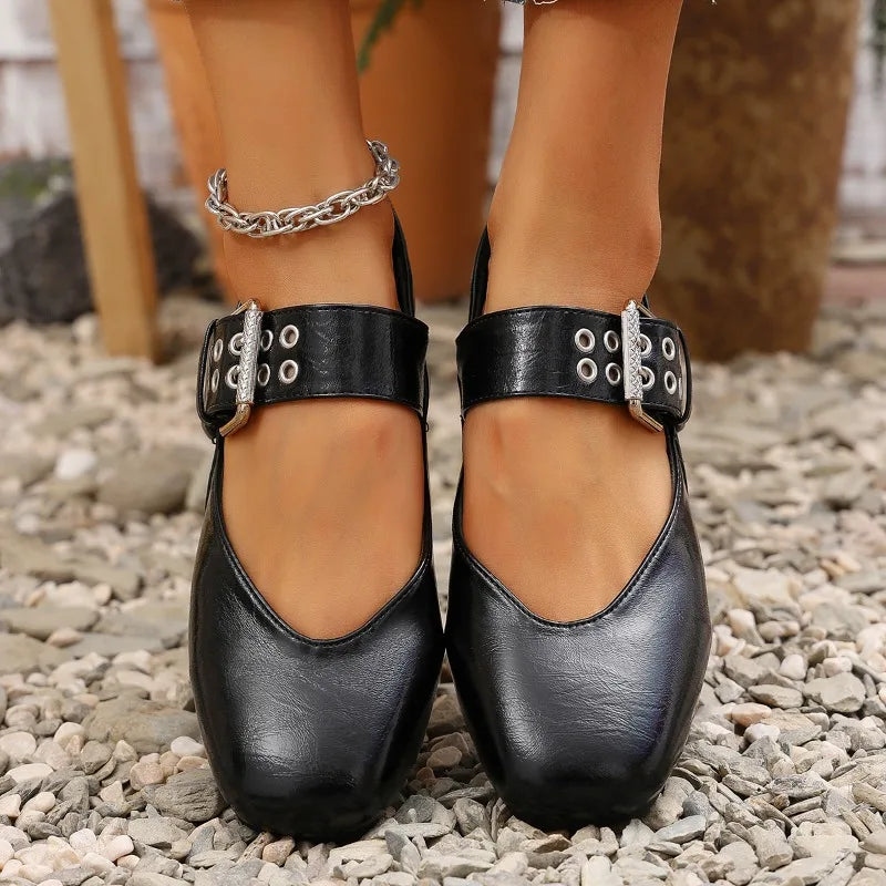 Black leather shoes with silver buckles worn on a rocky surface