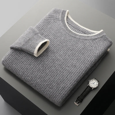 Folded gray sweater with a white trim on a dark surface, accompanied by a wristwatch.