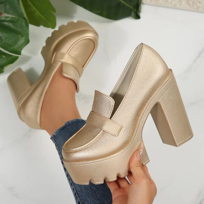Gold platform shoes being held with a white background