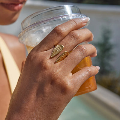 Hand holding a glass of iced drink with a gold ring, blurred background