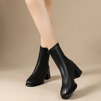Black ankle boots worn by a person on a beige background
