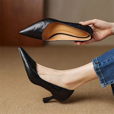 Black high-heeled shoes being held and worn on a beige background