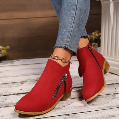 Red ankle boots with zippers worn with blue jeans on a wooden floor.