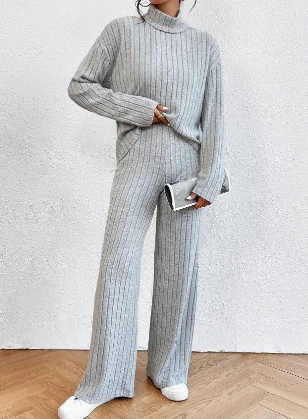 Person wearing a gray ribbed knit outfit with wide-leg pants against a white wall.