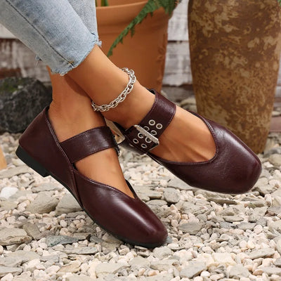 Brown leather shoes with buckles worn on a pebbled surface