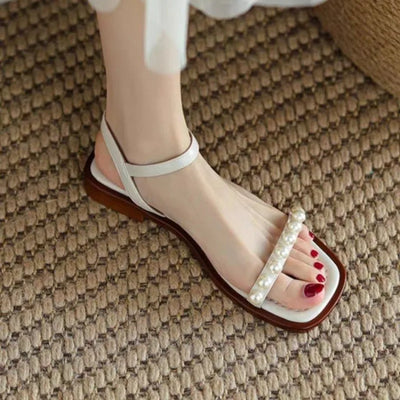 White sandal with pearl details on a textured carpet