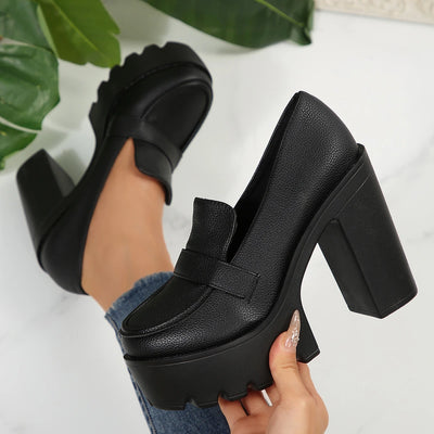 Black platform shoes being held with a white background and green leaves.