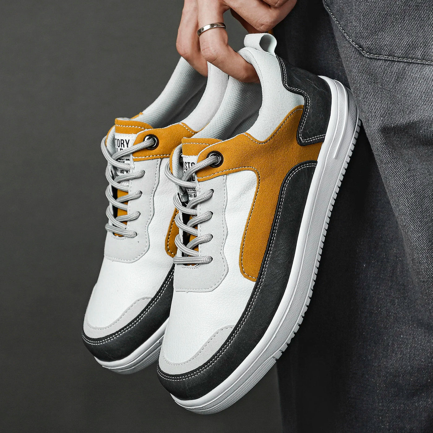 White and yellow sneakers with black soles held by a person against a dark background