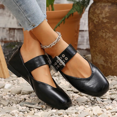 Black leather shoes with decorative straps worn on a rocky surface.