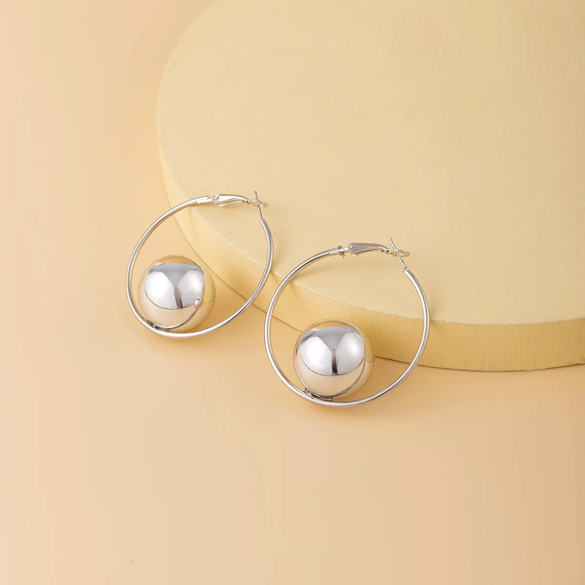 Silver hoop earrings with spherical ends on a beige background
