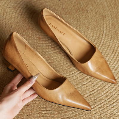 Pair of tan high heels on a textured surface with a hand touching one shoe.