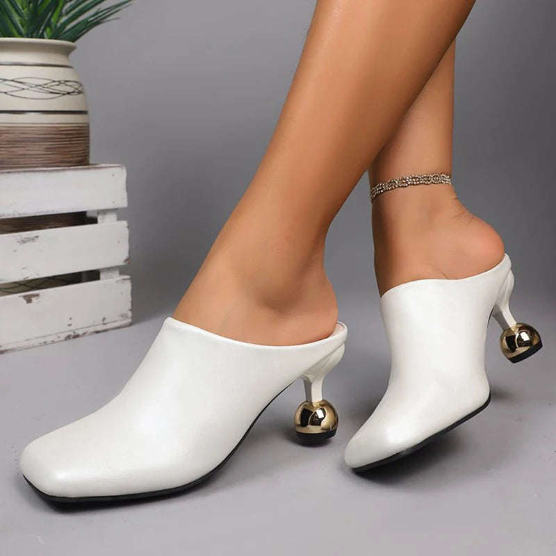 White high-heeled shoes with gold accents worn by a person on a gray background