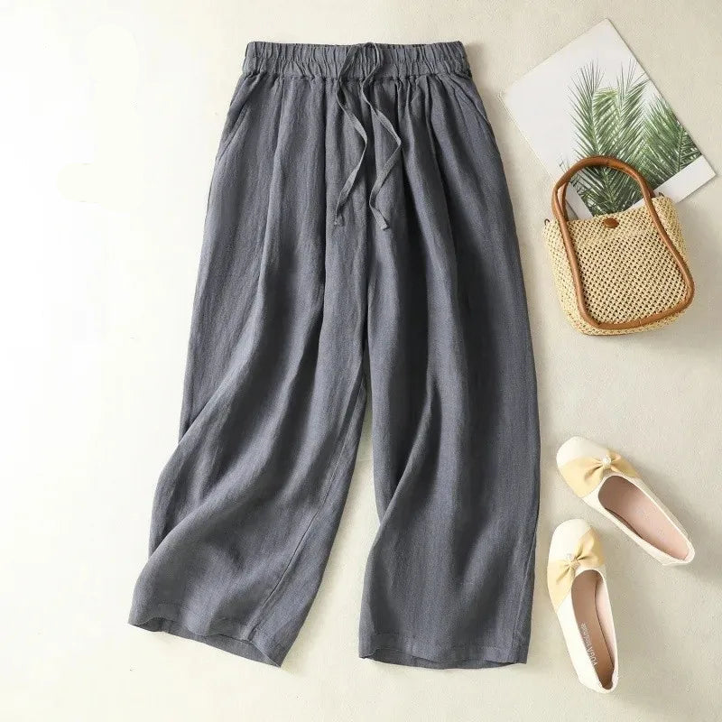 Gray wide-leg pants on a light surface with a small plant and woven bag.