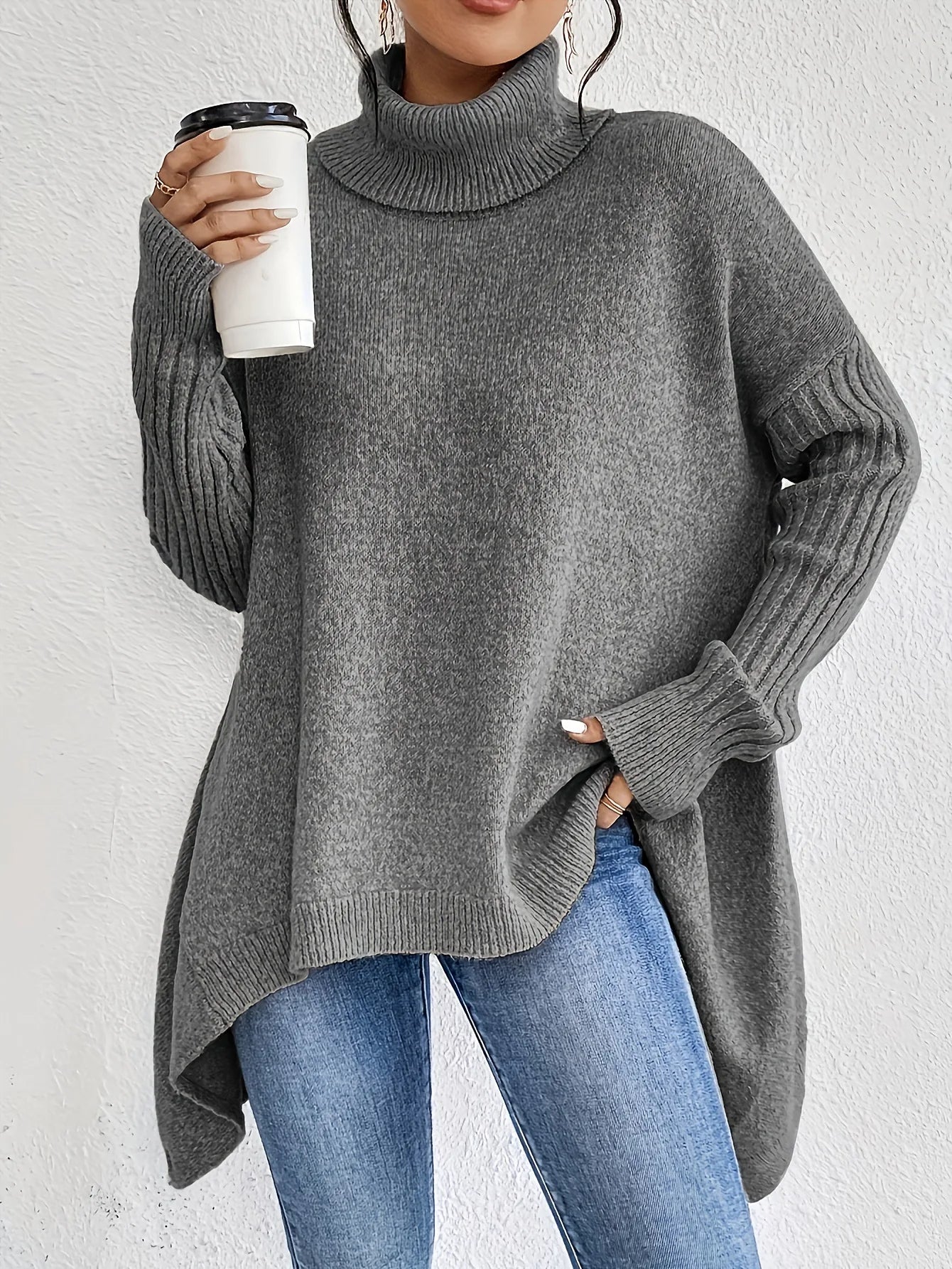 Person wearing a gray sweater and blue jeans, holding a white cup.