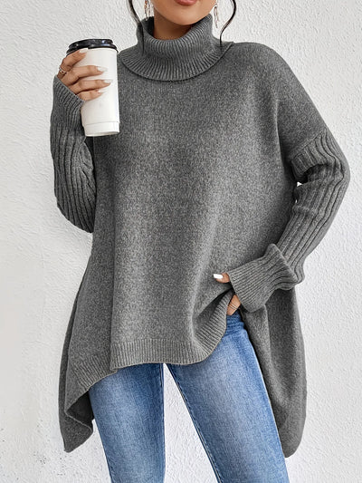 Person wearing a gray sweater and blue jeans, holding a white cup.