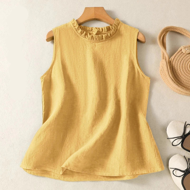 Yellow sleeveless top on a hanger with a woven basket and white shoes in the background.