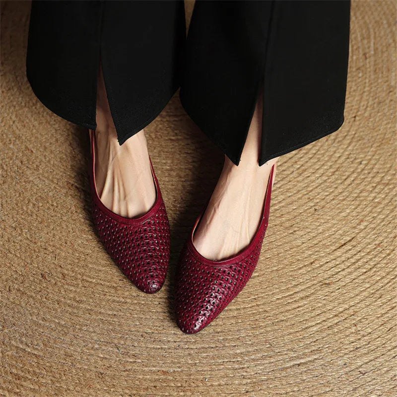 Red woven shoes worn with black pants on a textured surface