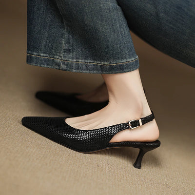Black kitten heel shoes worn with rolled-up jeans on a neutral background