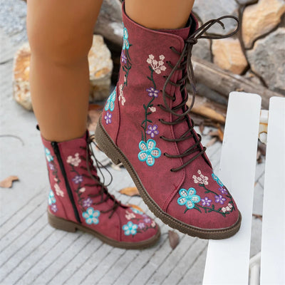 Red boots with floral embroidery worn by a person sitting on a stone surface.