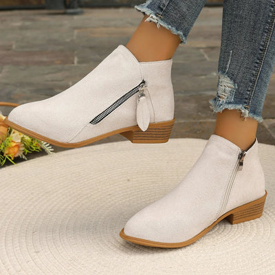 White ankle boots with brown soles worn by a person in jeans on a textured surface.