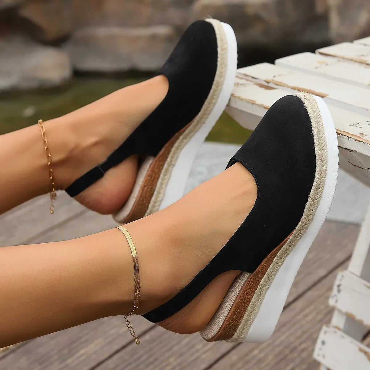 Black wedge sandals with white soles worn by a person on a wooden deck.