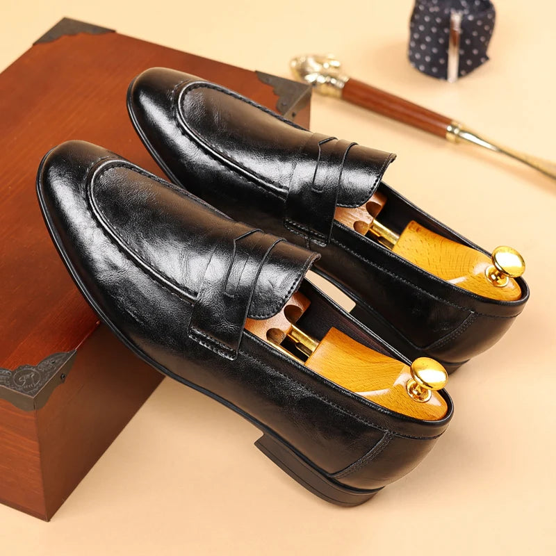 Pair of black leather loafers with gold accents on a wooden surface.