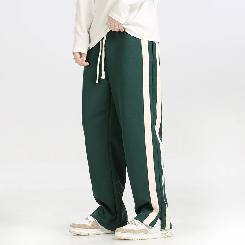 Green track pants with white stripes worn by a person on a white background