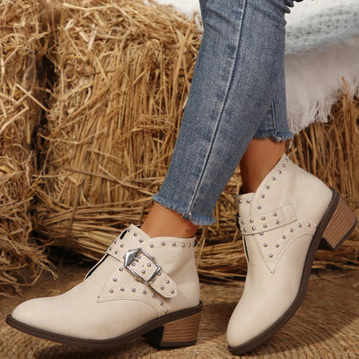 White studded boots with brown soles worn with blue jeans against a hay bale background