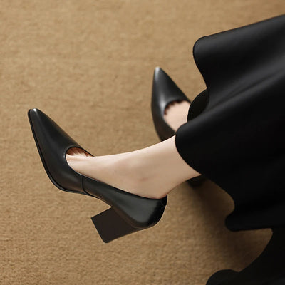Black high-heeled shoes worn with a black skirt on a brown background