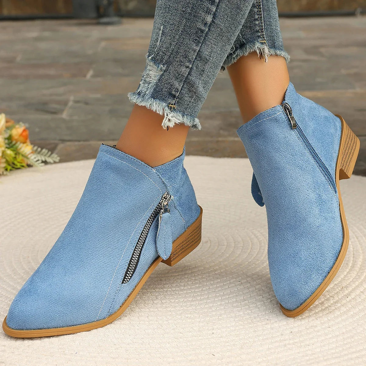 Blue denim ankle boots with brown soles worn by a person, on a textured surface.