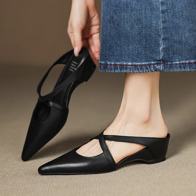 Black pointed-toe shoes worn with blue jeans on a neutral background