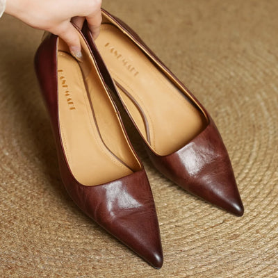 Pair of brown pointed-toe shoes with tan insole on a textured surface